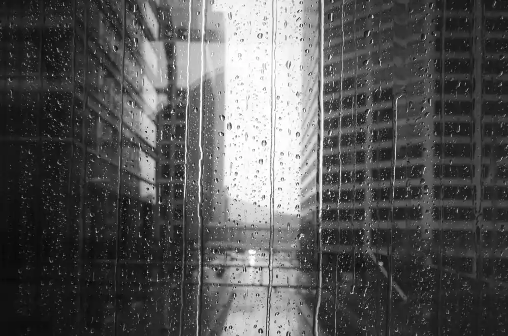 Rain running down a window, office towers blurred behind it