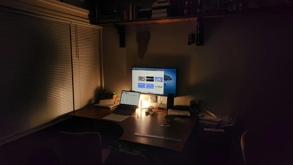 A dark room at night, lit only by a monitor and a small desk lamp